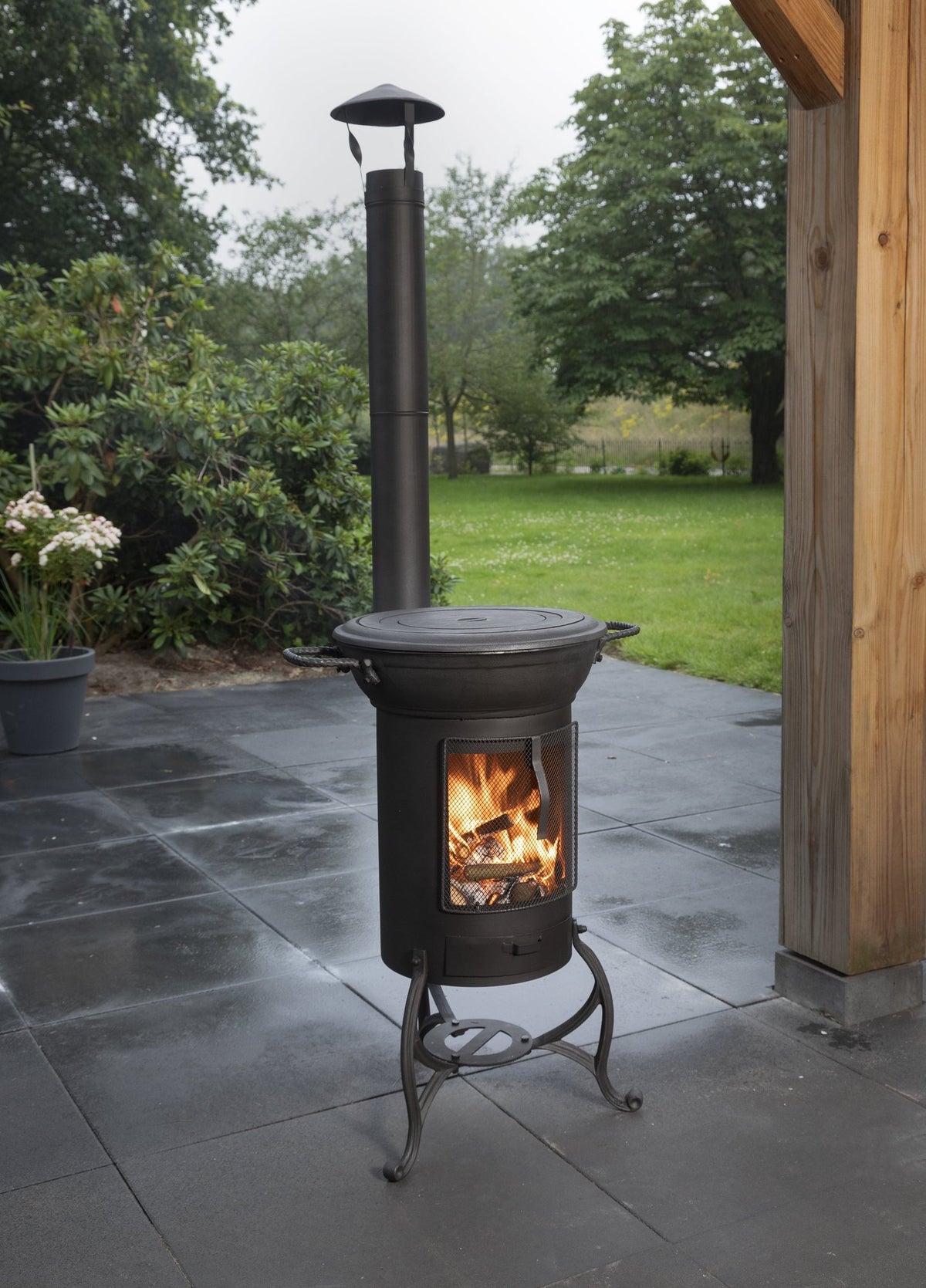 Poêle d'extérieur Globe-fire Krakatau - en situation sur une terrasse sous une pergola, avec sa flamme visible