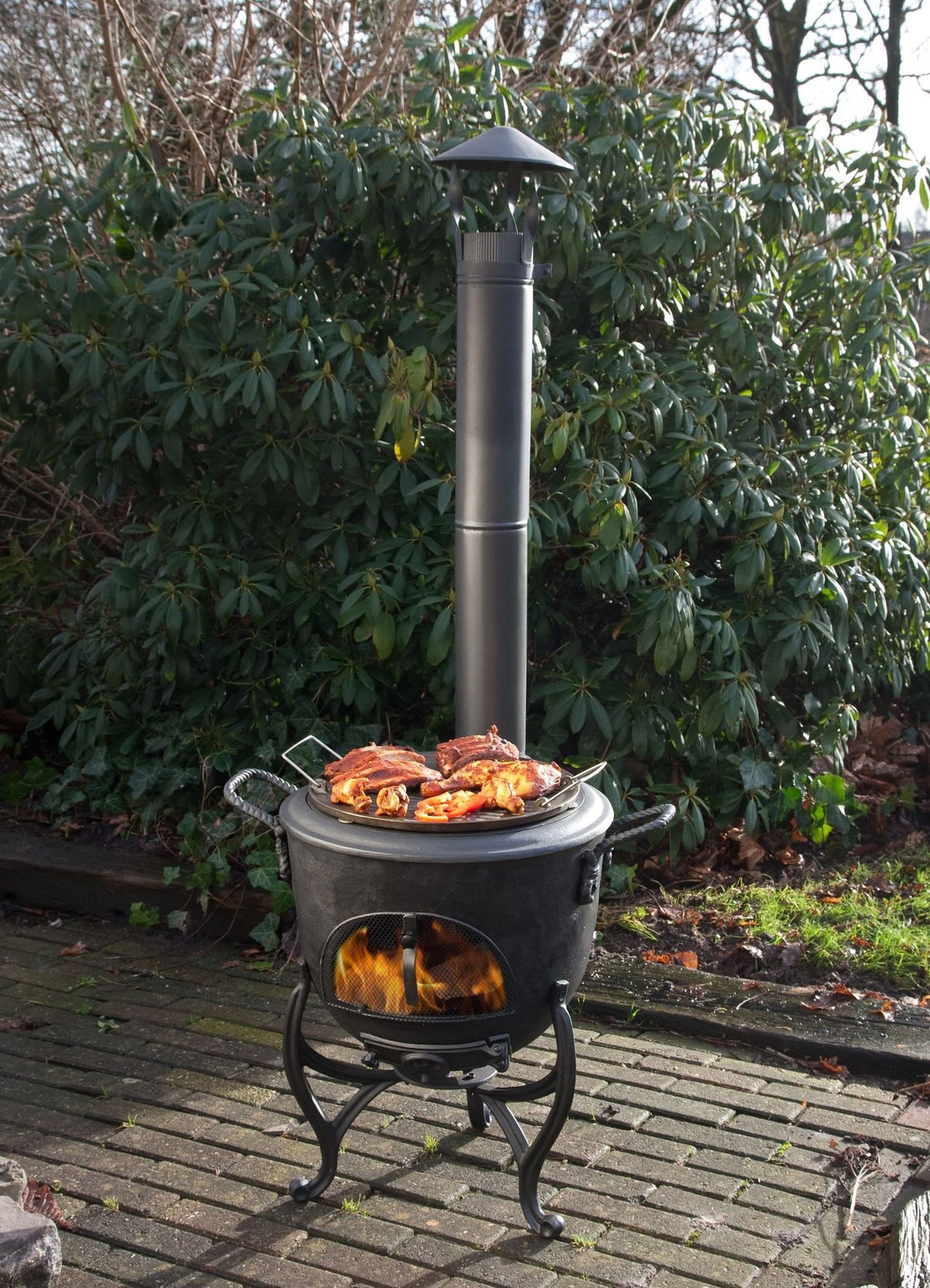 Poêle d'extérieur Globe-fire Volcano - en situation sur une terrasse pavée, avec ses tuyaux et son capuchon pare-pluie